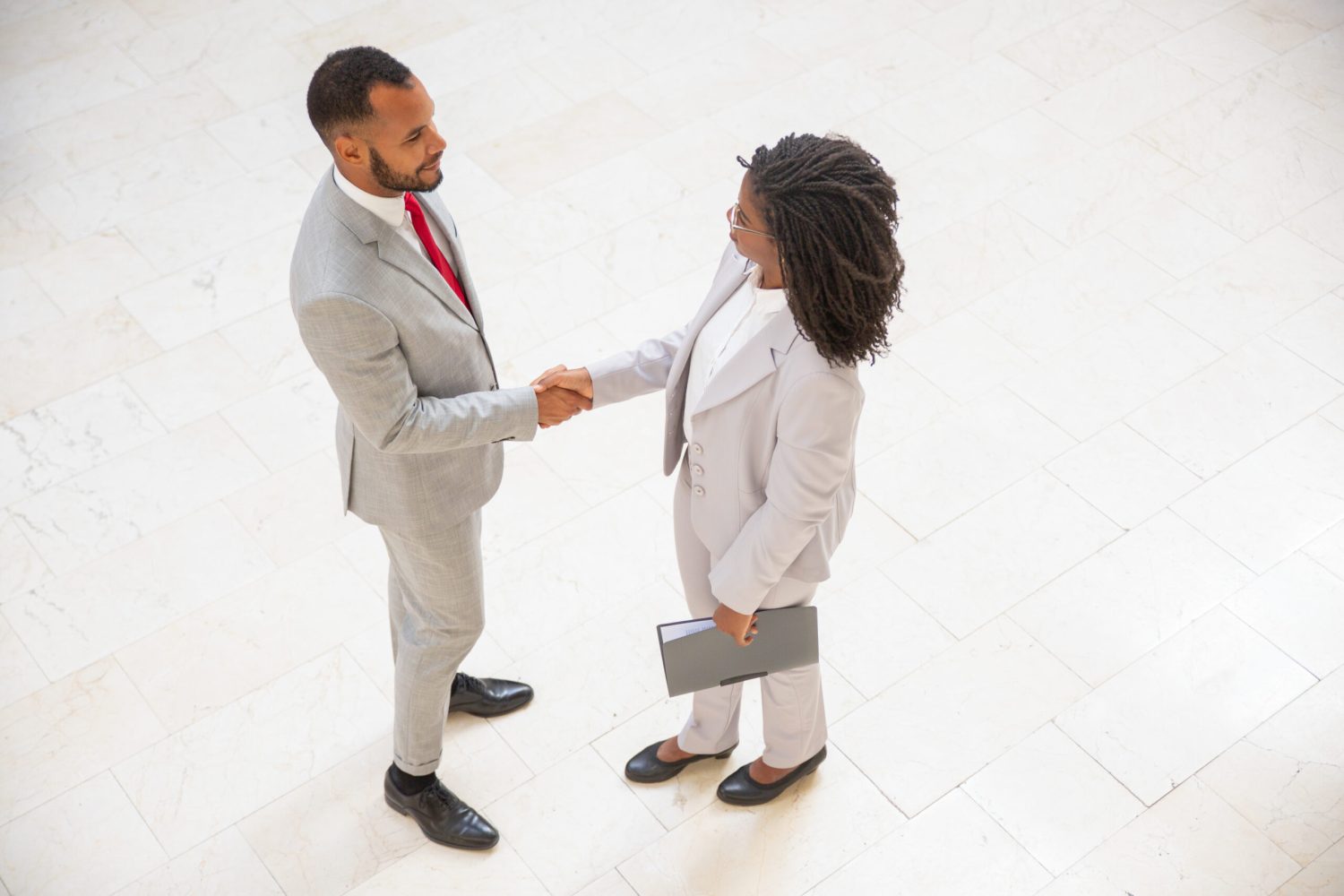Business partners greeting each other in office hallway Business partners greeting each other in office hallway. Diverse business man and woman standing and shaking hands. Business meeting concept